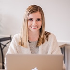 A smiling Ashley Mason seated at a desk with an open laptop