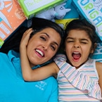 A smiling Shalini Samtani lying amid toys with a young girl next to her