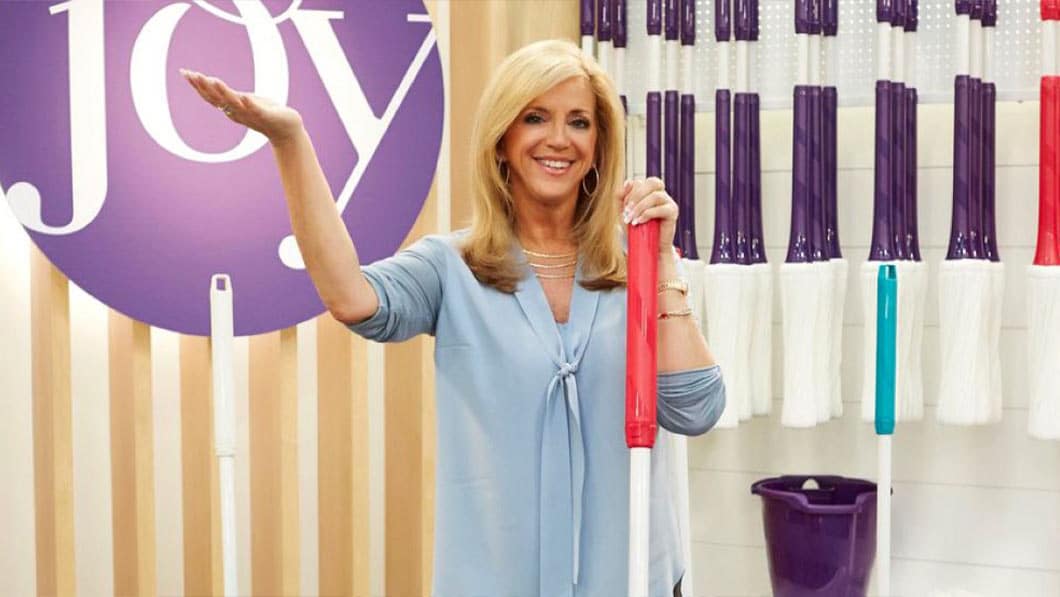 Photo of entrepreneur Joy Mangano holding up one hand and a mop in the other