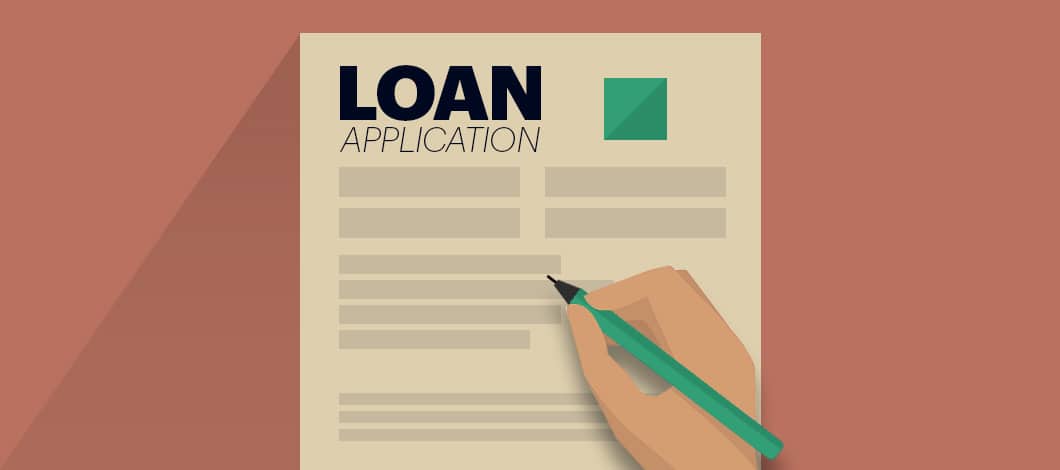 A hand holds a pen to fill out an application form labeled “Loan Application.”