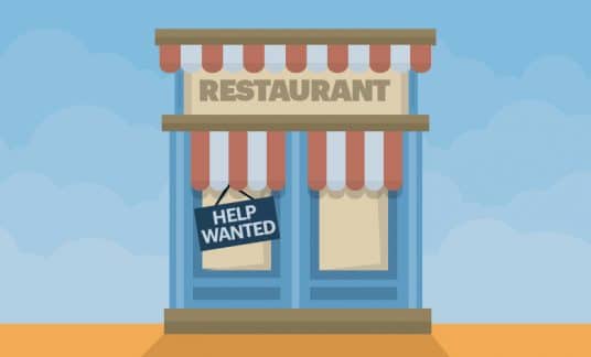 A “Help Wanted” sign hangs in the front window of a restaurant.