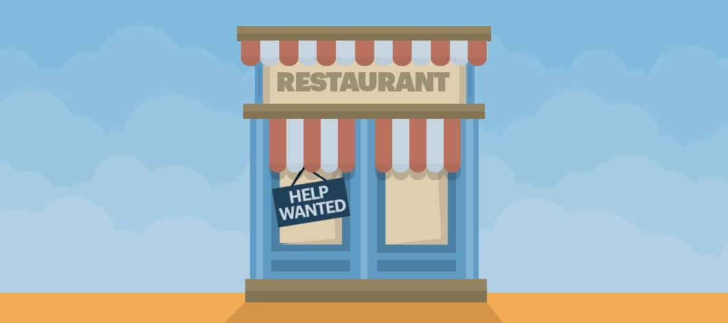 A “Help Wanted” sign hangs in the front window of a restaurant.