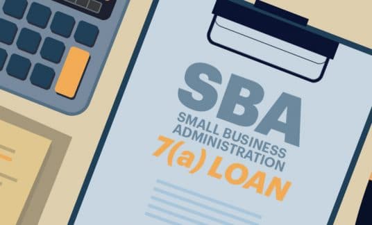 A clipboard holding a form that reads “SBA 7(a) loan” sits on a desk next to a pen and a calculator.