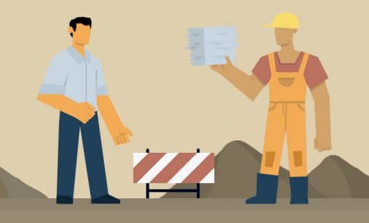 At a construction site, a contractor wearing a hard hat hands a stack of pay applications for construction to a business person.