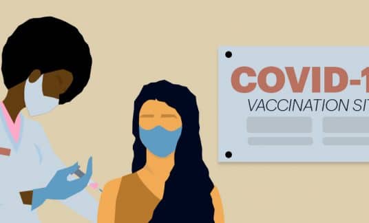 A masked person is about to get a shot from a masked medical professional. The background reads “COVID-19 Vaccination Site.”