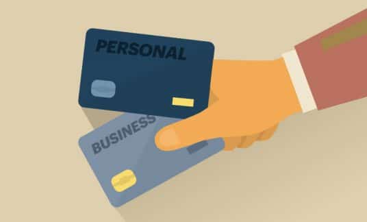 A hand holds two credit cards. One is labeled “Personal” and the other is labeled “Business.”