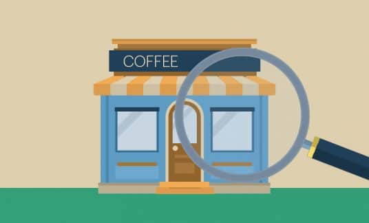 A giant magnifying glass inspects a small coffee shop.