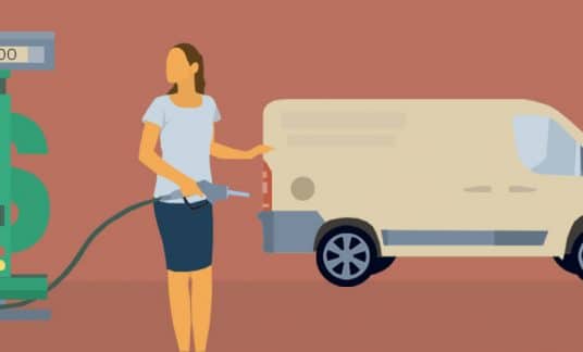 A woman fills her work van with gas. She looks at the gas pump, which is shaped like a dollar sign.