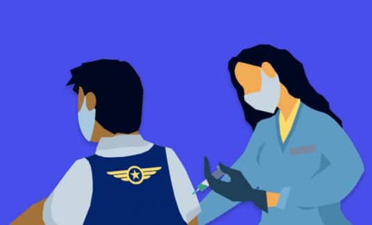 An airline employee wearing a mask gets a vaccination shot from a masked medical professional.