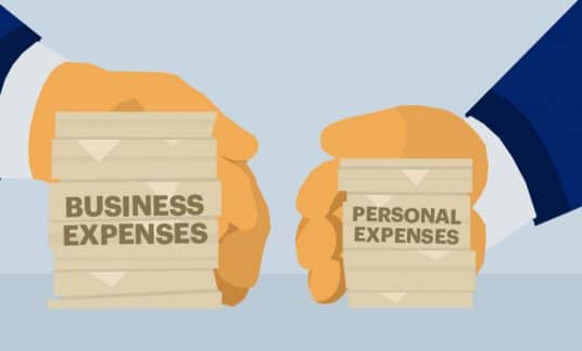 A pair of hands separate two stacks of paper, one labeled “Business Expenses” and the other marked “Personal Expenses.”