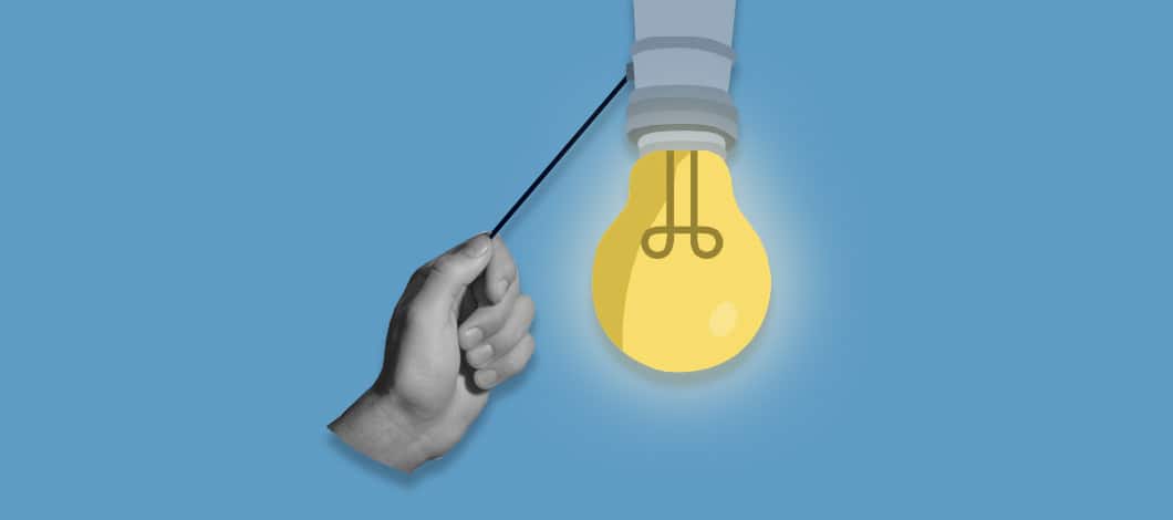 A hand pulls on a metal chain to turn on a light bulb.