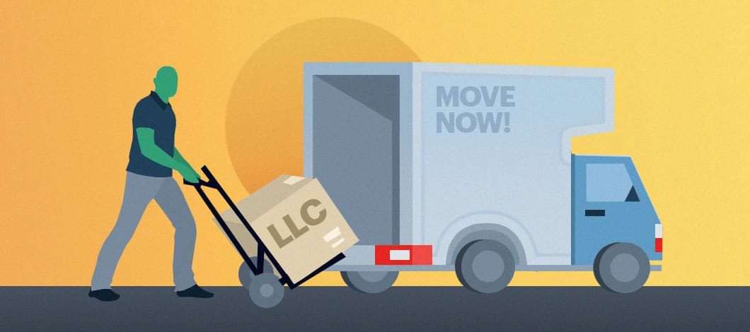 A mover with a hand truck rolls a big box marked “LLC” toward a moving truck.